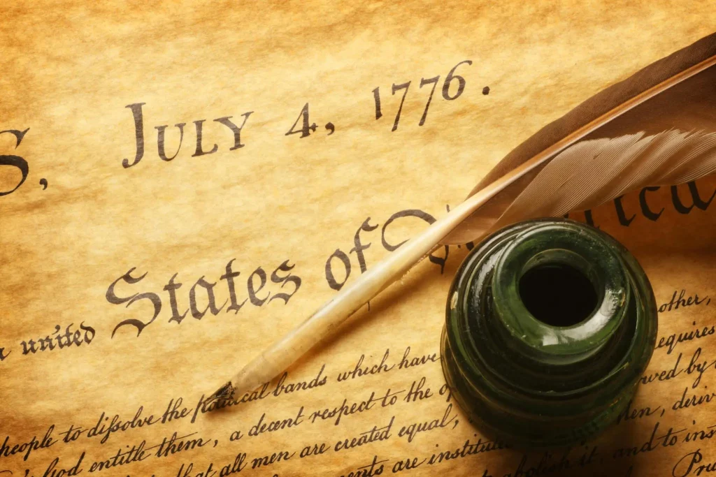 A feather quill and inkwell sitting on top of the American Declaration of Independence